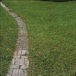 Brick paver path curving through a green lawn toward a house.