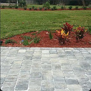 Paver patio set into a back lawn with a red-mulch planting bed behind it.