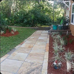 Stone walkway through a shaded front yard with a fresh mulch bed and shrubs.