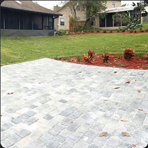 Newly laid grey paver patio set into a back lawn with a planting bed behind.